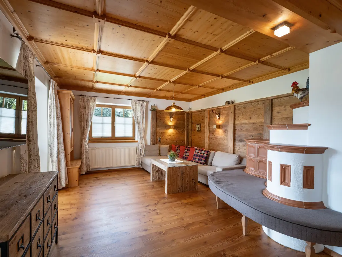 Rustikales Wohnzimmer im Tiroler Stil mit einer großen Kassettendecke aus Holz, einer gemütlichen Ecksitzgruppe, einem Kachelofen und einem massiven Holzboden — Ferienwohnung Gafalhof Going Tirol